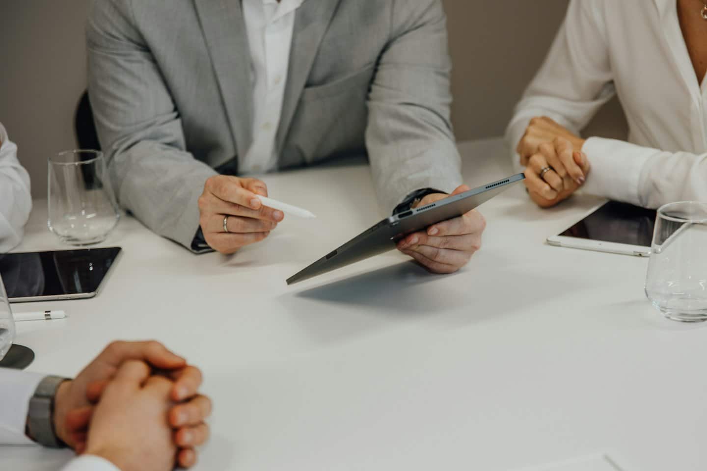 Person in grey suit presents on tablet at white conference table.